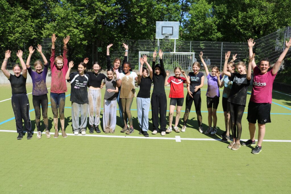 Gruppe von Schülern auf einem Sportplatz feiert den Abschluss eines Wettkampfs.