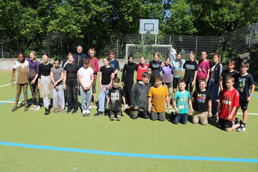 Gruppe von Kindern und Erwachsenen auf einem Sportplatz, vor einem Tor.