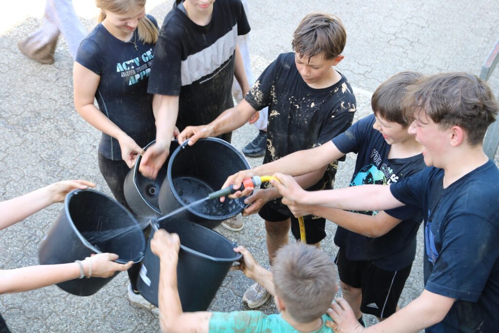 Kinder füllen gemeinsam Wasser in mehrere Eimer.