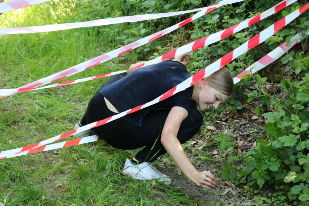 Ein Mädchen kniet unter rot-weißen Absperrbändern und schaut zu Boden.