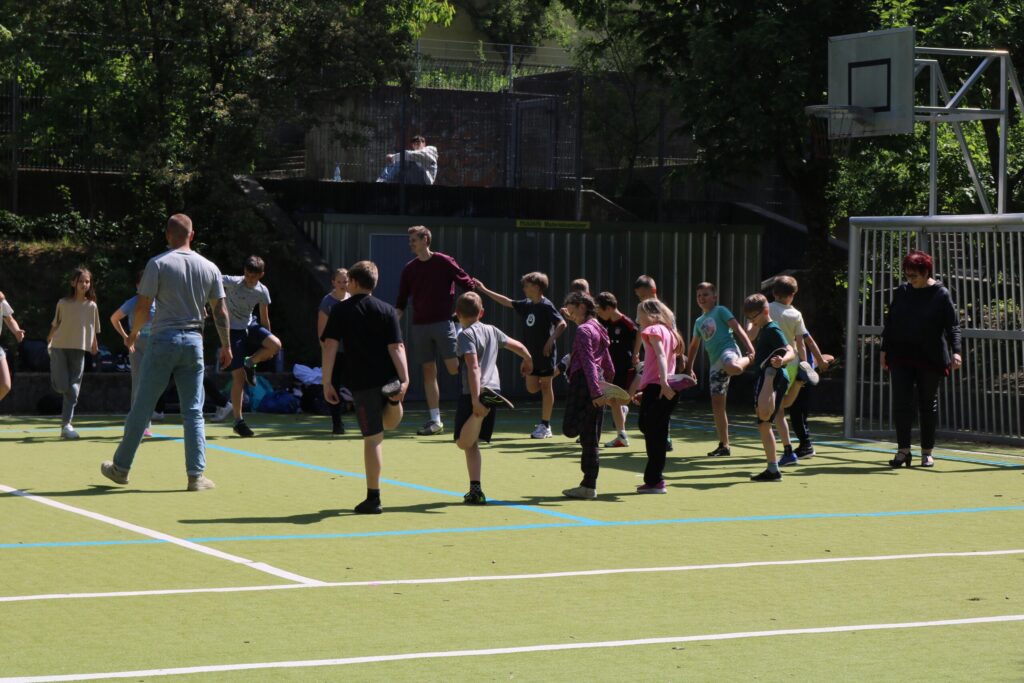 Gruppentraining von Kindern auf einem Sportplatz, einige stehen, andere dehnen.