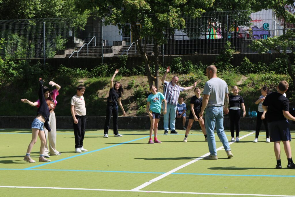 Schülerinnen und Schüler spielen auf einem Sportplatz in einer Gruppenaktivität.
