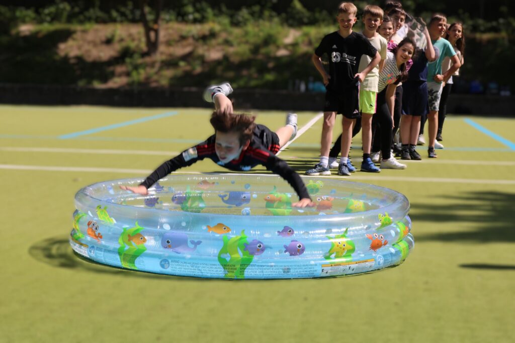 Ein Kind springt ins Wasser eines aufblasbaren Pools, während andere zuschauen.