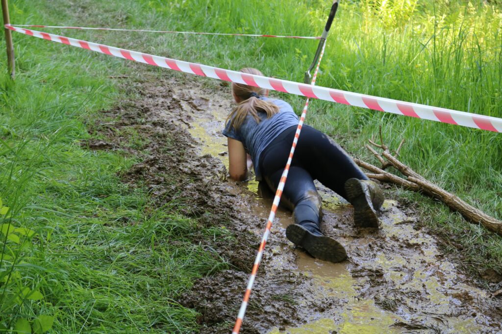 Schülerin kriecht durch einen schlammigen Weg, umgeben von Absperrband.