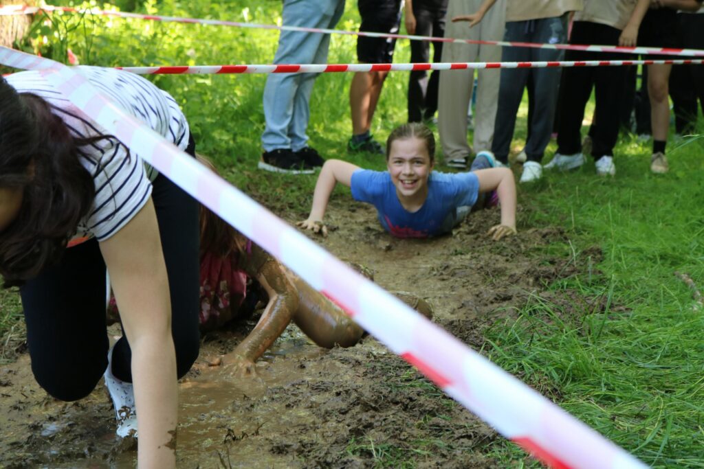 Schüler kriechen durch einen schlammigen Hindernisparcours im Freien.
