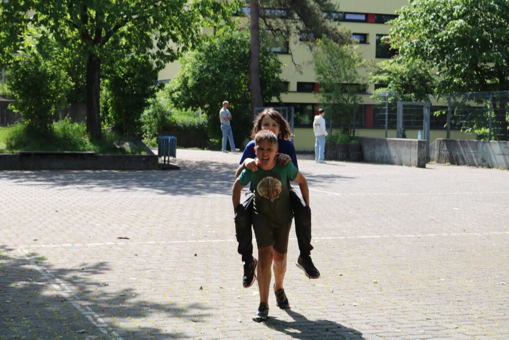 Ein Junge trägt ein Mädchen auf dem Rücken in einem Schulhof.