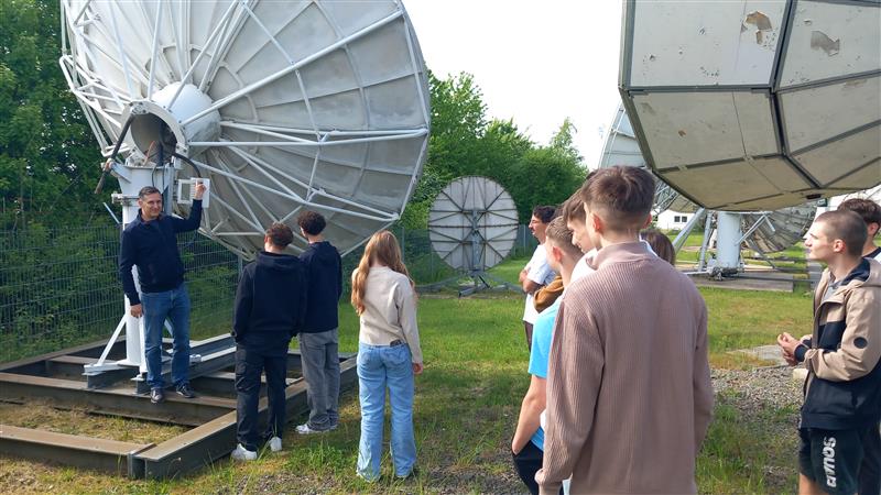 Gruppe von Schülern bei einer Technikführung an Satellitenschüsseln im Freien.