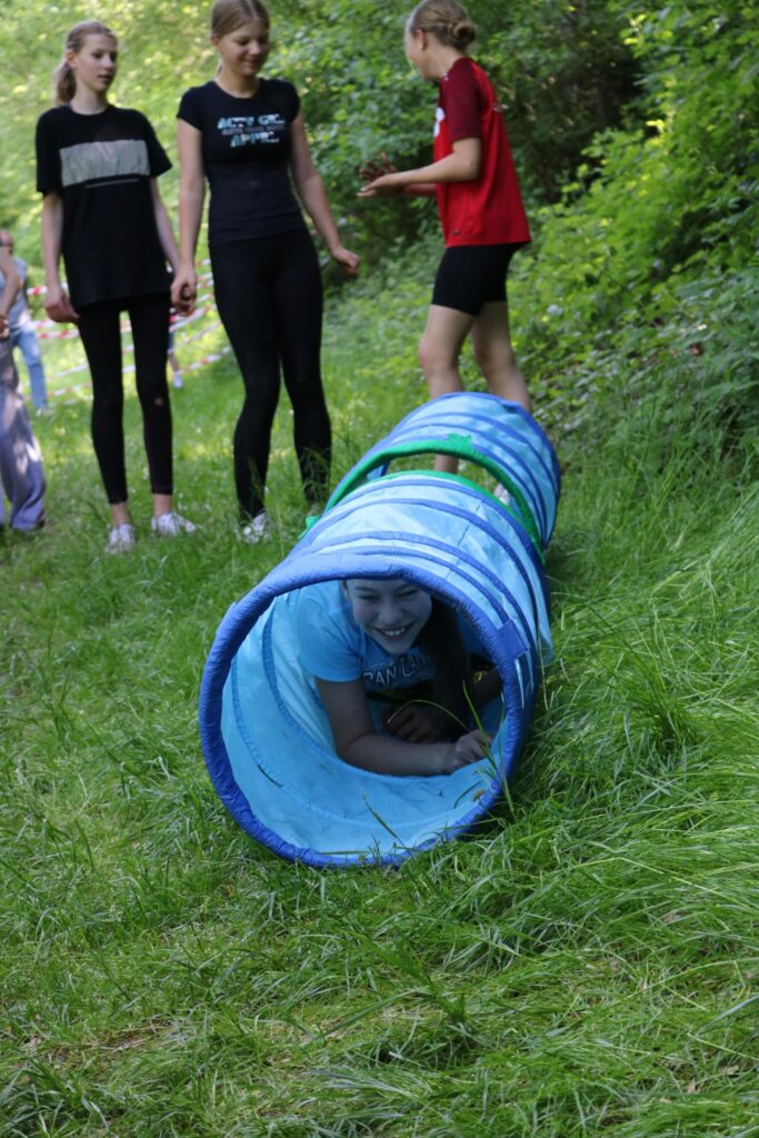 Kinder spielen im Freien und kriechen durch einen blauen Spieltunnel.