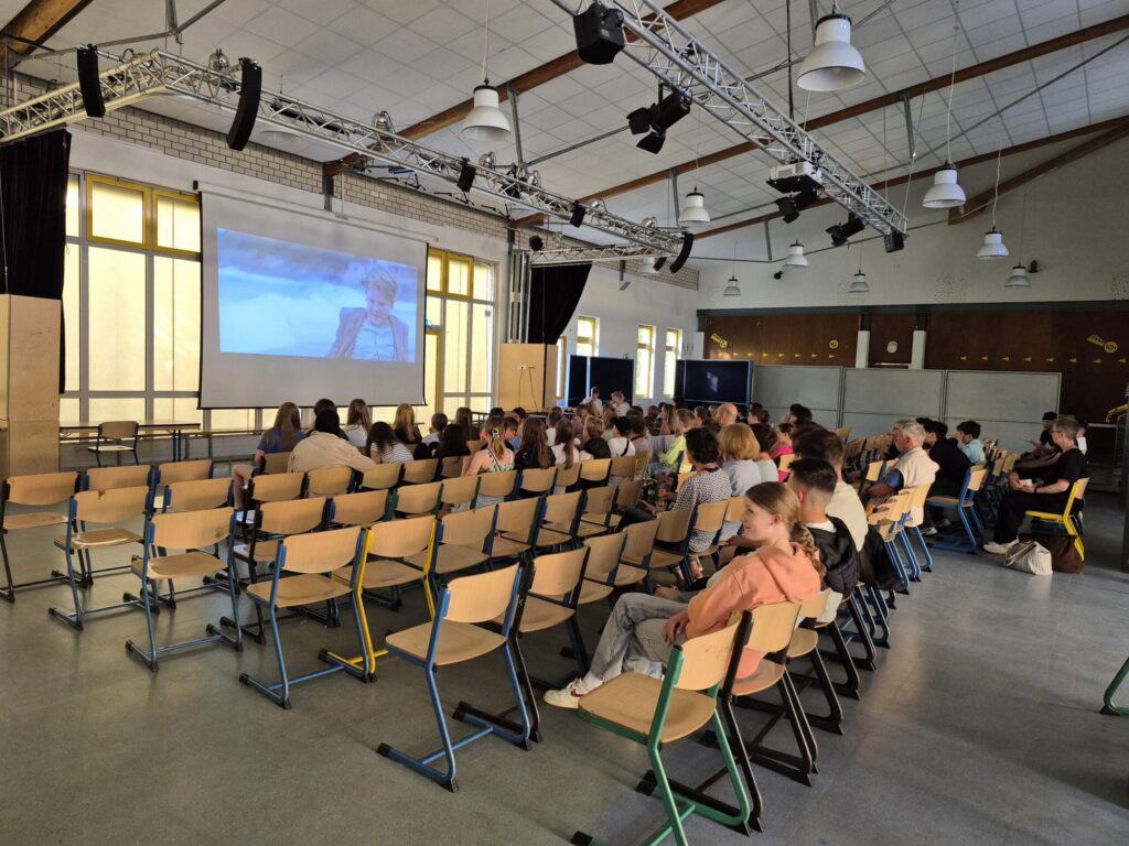 Schüler sitzen in einem Saal vor einer Leinwand.