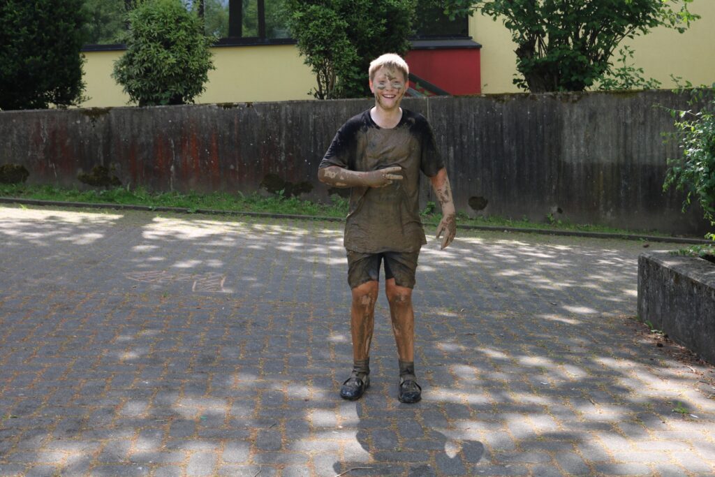 Ein Junge steht schmutzig und voller Schlamm auf einem Gehweg.