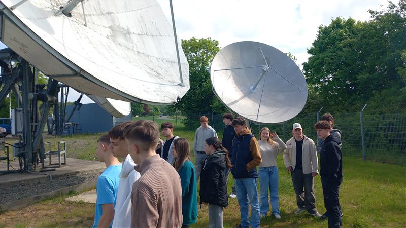 Schülergruppe besichtigt Satellitenschüsseln im Freien.