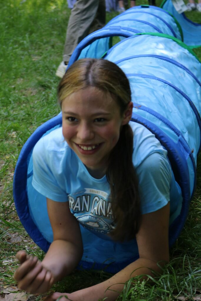 Mädchen kriecht lächelnd durch einen blauen Tunnel im Freien.