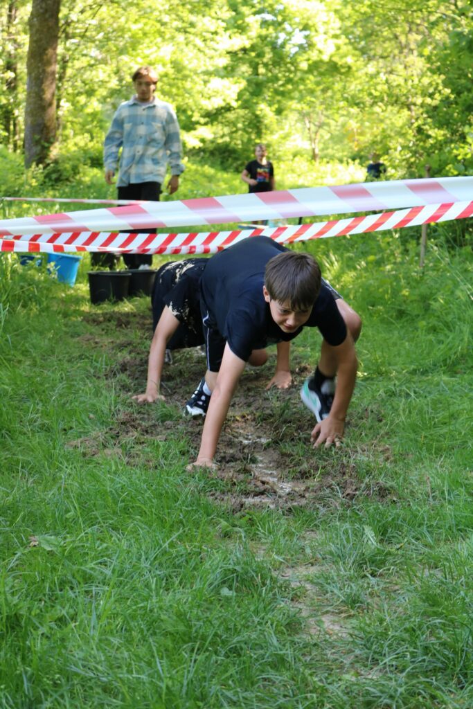 Ein Junge krabbelt auf dem Boden, umgeben von grüner Wiese und plakativen Absperrbändern.