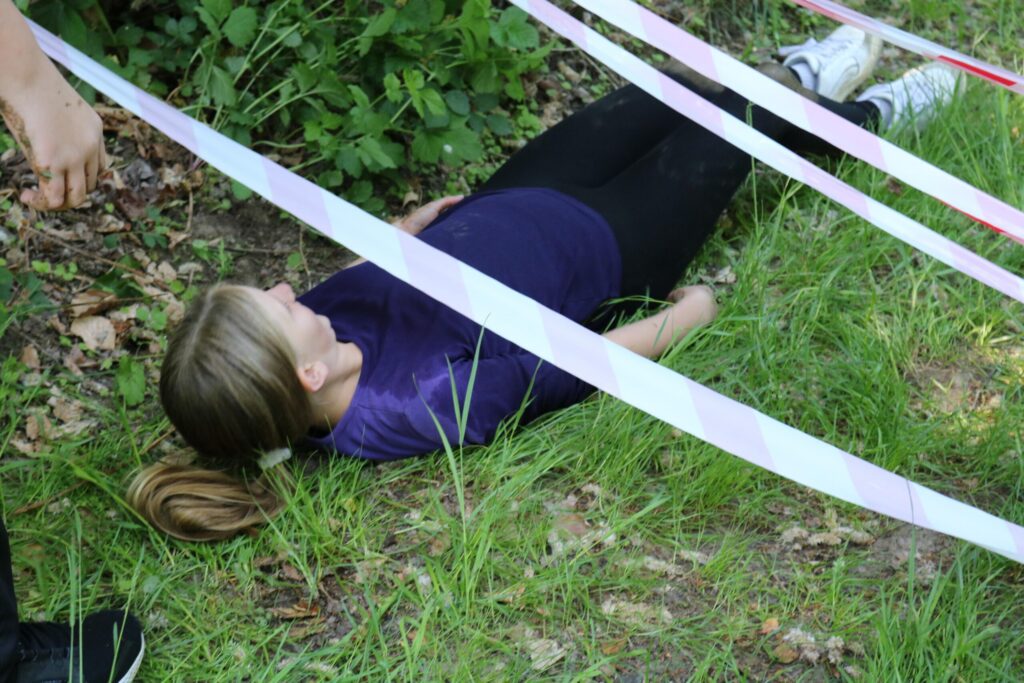 Eine Person liegt auf dem Boden, umgeben von Absperrbändern und Gras.