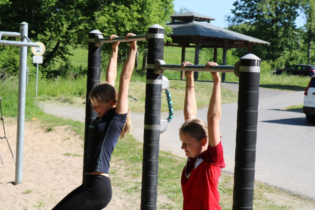 Zwei Mädchen machen Klimmzüge an einem Sportgerät im Freien.
