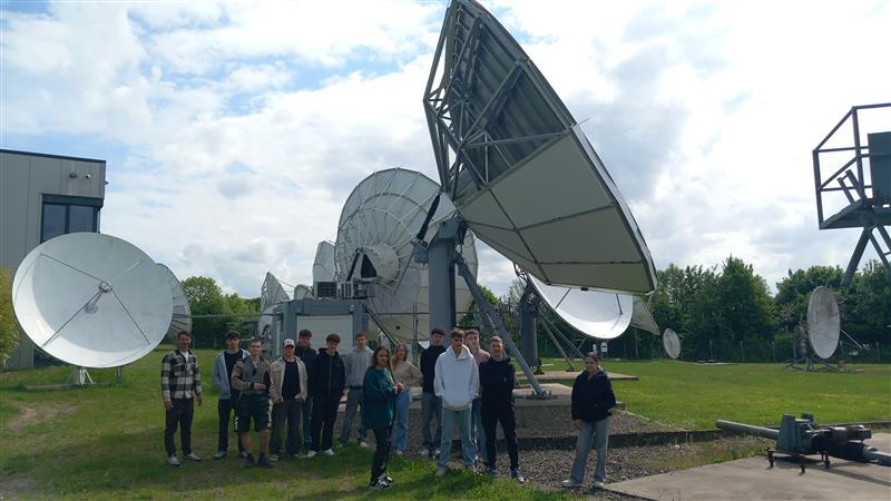 Gruppe von Schülern vor Satellitenschüsseln und Antennen im Freien.