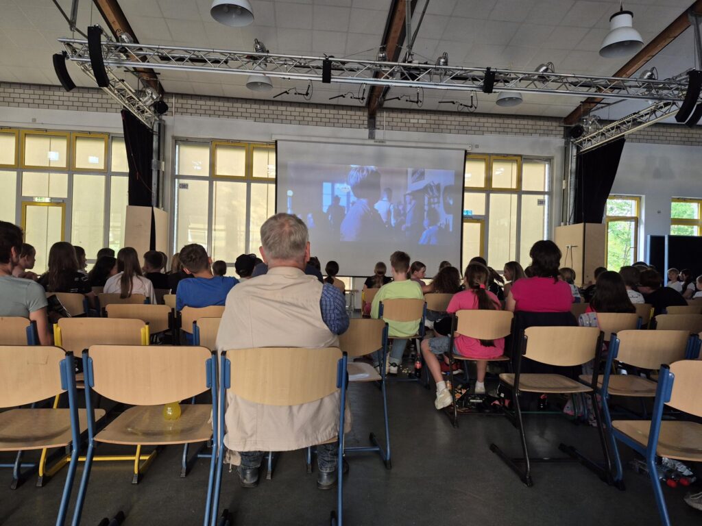 Schülerinnen und Schüler sitzen im Raum, schauen einen Film auf der Leinwand.