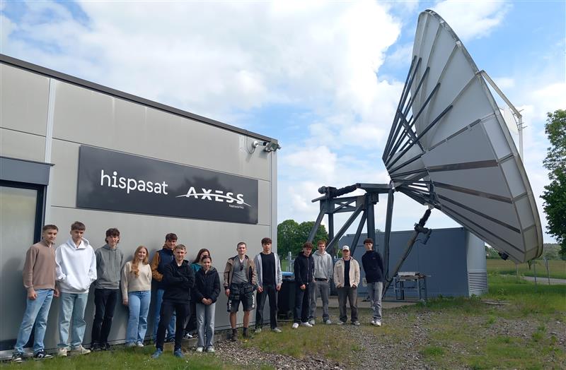 Gruppe von Schülern vor einem Gebäude mit einer großen Satellitenschüssel.