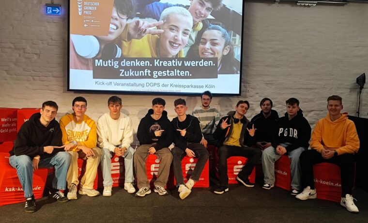 Gruppe junger Menschen sitzt auf einer Bühne mit einem Präsentationsbild im Hintergrund.