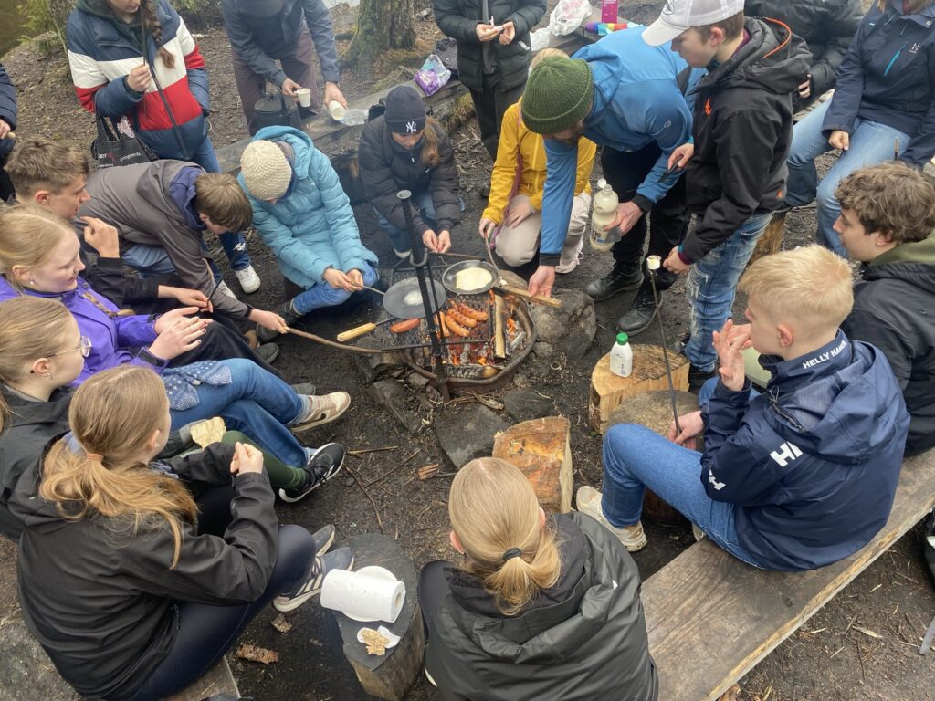 Gruppe von Schülern versammelt um ein Lagerfeuer, Essen zubereitend.