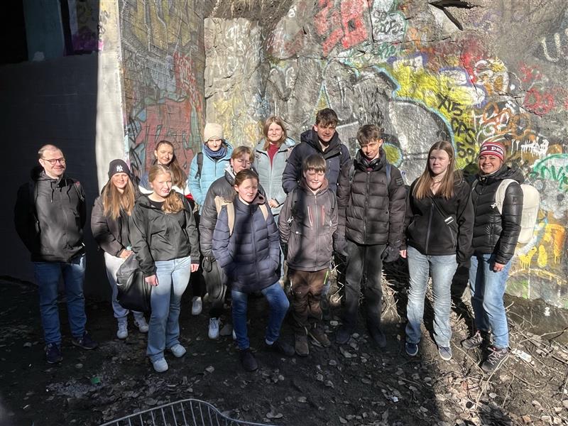 Gruppe von 13 Personen vor einer bunten Graffiti-Wand im Freien.