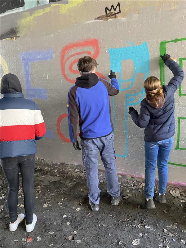 Drei Personen sprühen bunte Graffiti an eine Wand.
