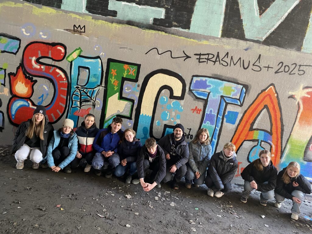 Gruppe von Schülern vor einer bunten Graffiti-Wand, alle lachen und posieren.