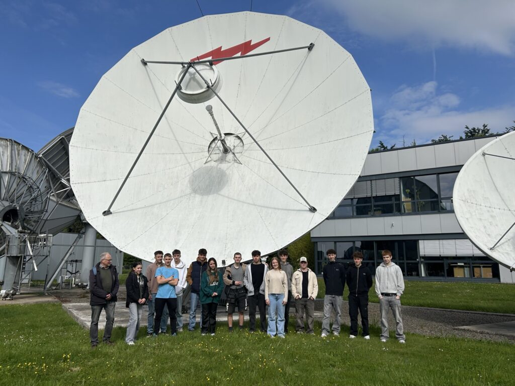 Gruppe von Personen steht vor großen Satellitenschüsseln im Freien.