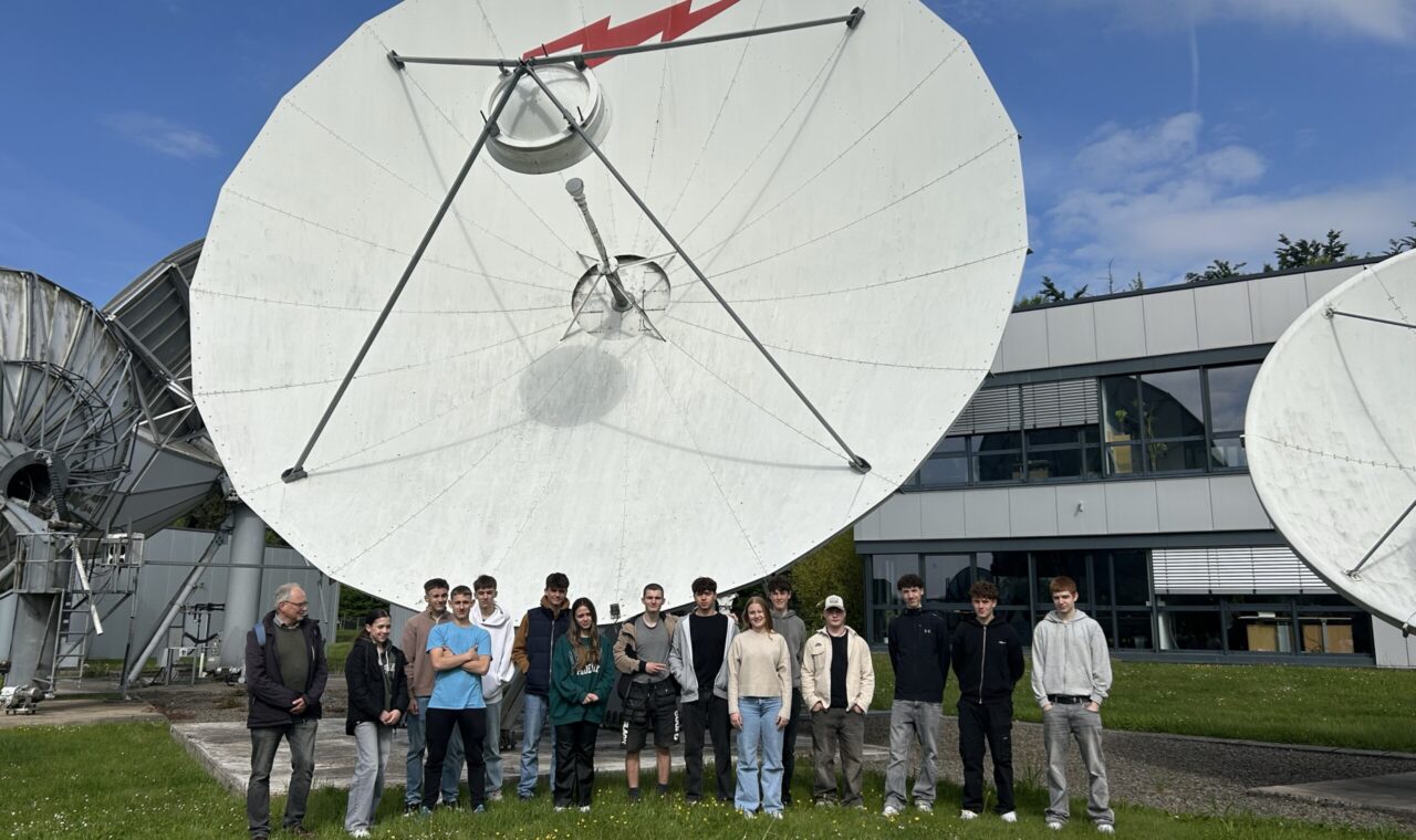 Gruppe von Personen steht vor großen Satellitenschüsseln im Freien.