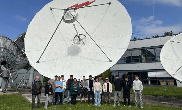Gruppe von Personen steht vor großen Satellitenschüsseln im Freien.
