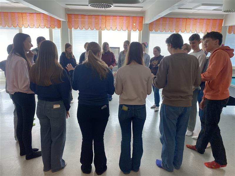 Gruppe von Schülern steht im Kreis und interagiert miteinander.