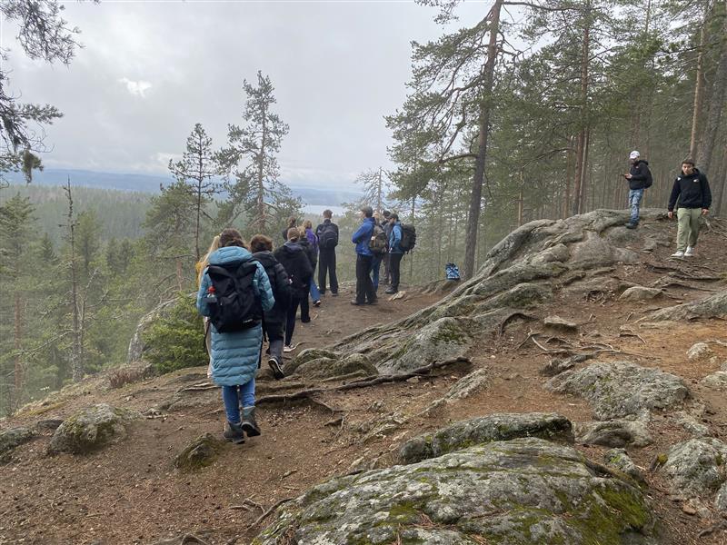 Schülergruppe wandert auf einem Waldweg zwischen Bäumen und Felsen.