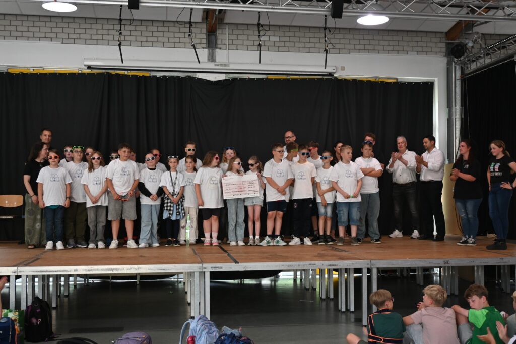 Schüler stehen auf der Bühne, präsentieren zusammen in weißen T-Shirts.