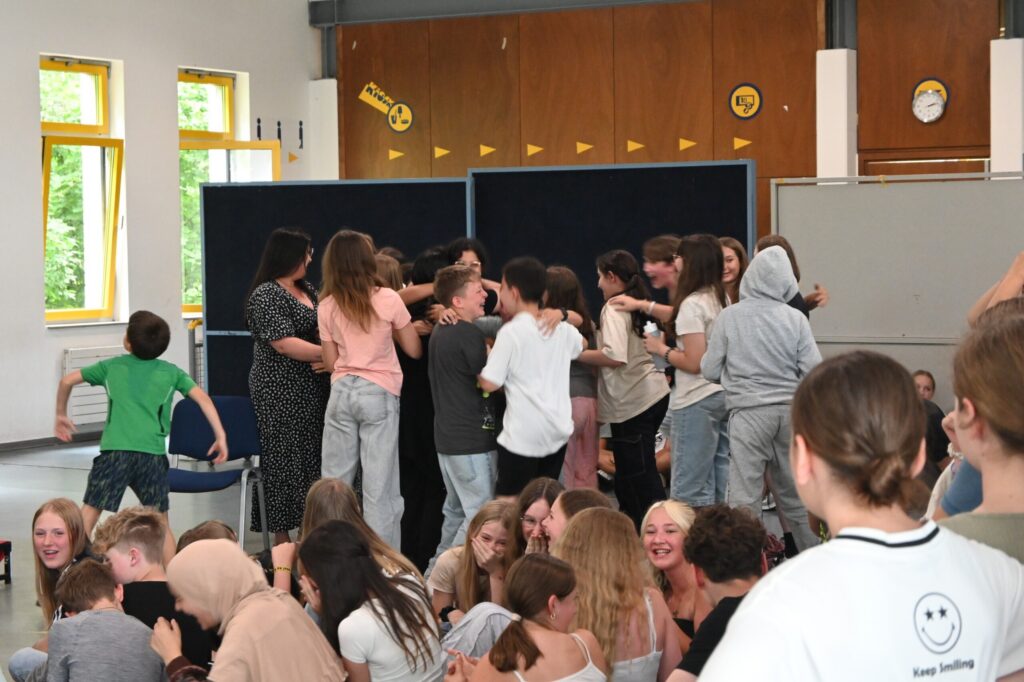Schüler stehen in Gruppen und interagieren in einem hellen Klassenraum.