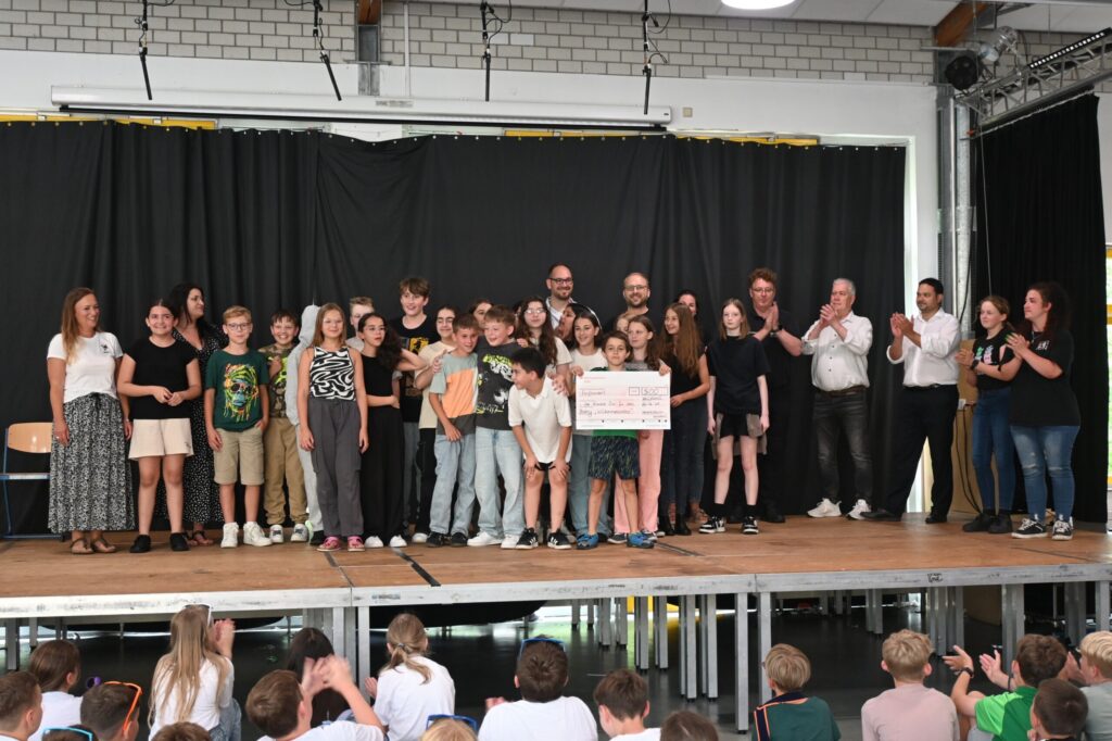 Gruppenszene auf einer Bühne mit Schülern und Lehrern bei einer Veranstaltung.