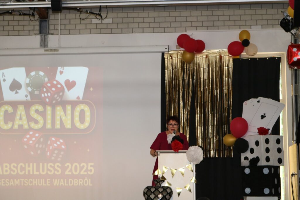 Schulleiterin Kirsten Wallbaum hält ihre Rede am Rednerpult, umgeben von aufwändiger Casino-Dekoration mit Spielkarten und Girlanden.