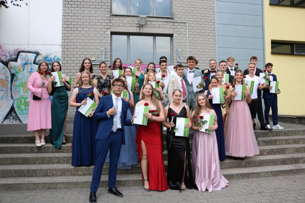Gruppenfoto einer weiteren Abschlussklasse auf der Freitreppe vor der Schule – Urkunden und Rosen in den Händen, festliche Stimmung im Bild eingefangen.