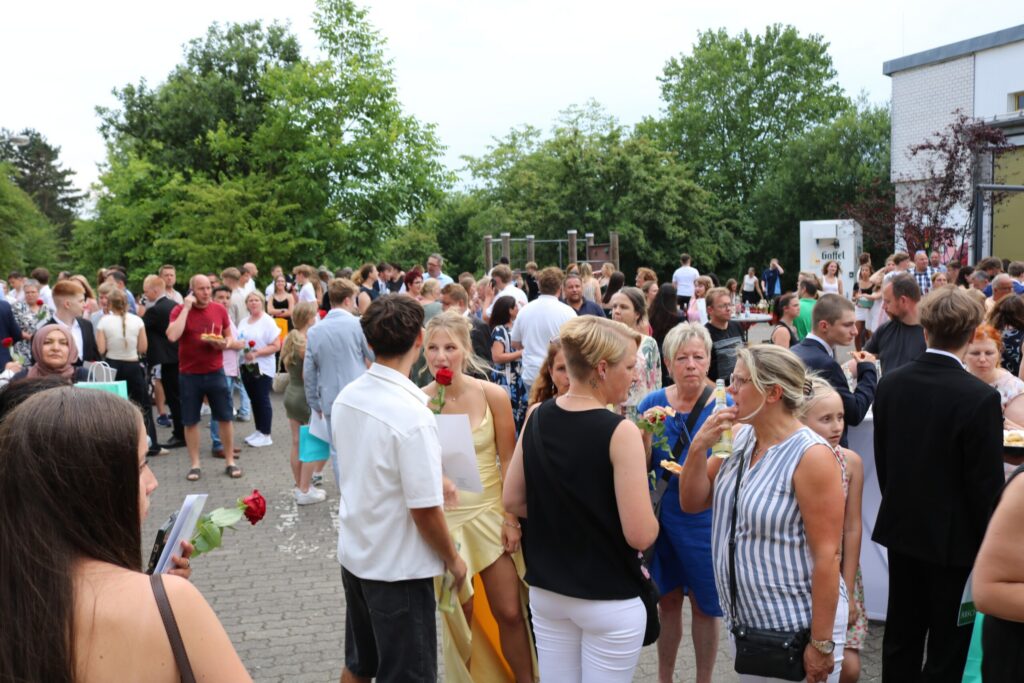 Feierliche Stimmung auf dem Schulhof: Hunderte Gäste und Absolvent:innen versammeln sich bei sommerlichem Wetter zum geselligen Ausklang der Abschlussfeier.