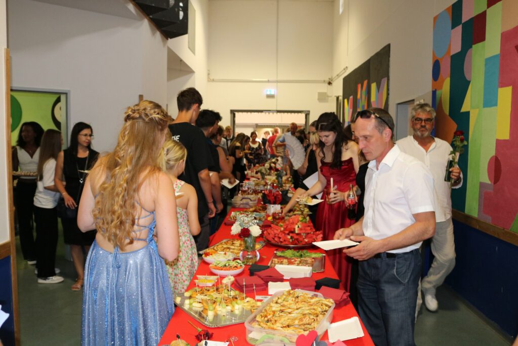 Blick auf das reichhaltige Buffet im Schulflur – Gäste und Absolvent:innen bedienen sich an einer langen Tafel mit süßen und herzhaften Snacks.