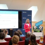 Moderatorin der Verleihungsveranstaltung des Berufswahl-Siegels 2025 spricht vor Publikum. Auf der Präsentationsfolie sind Programmpunkte und der stilisierte Siegel-Roboter zu sehen.