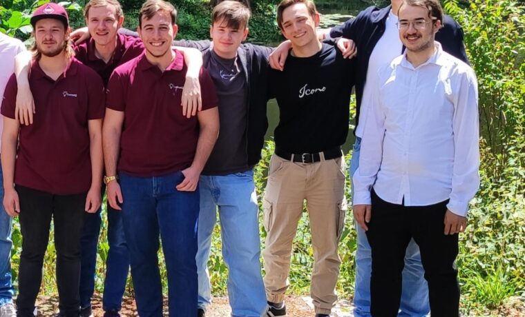 Gruppenfoto beider Teams der Gesamtschule Waldbröl vor grüner Kulisse im Schlosspark Eller: Die Jugendlichen stehen entspannt nebeneinander, einige mit verschränkten Armen, andere mit lachendem Blick zur Kamera.