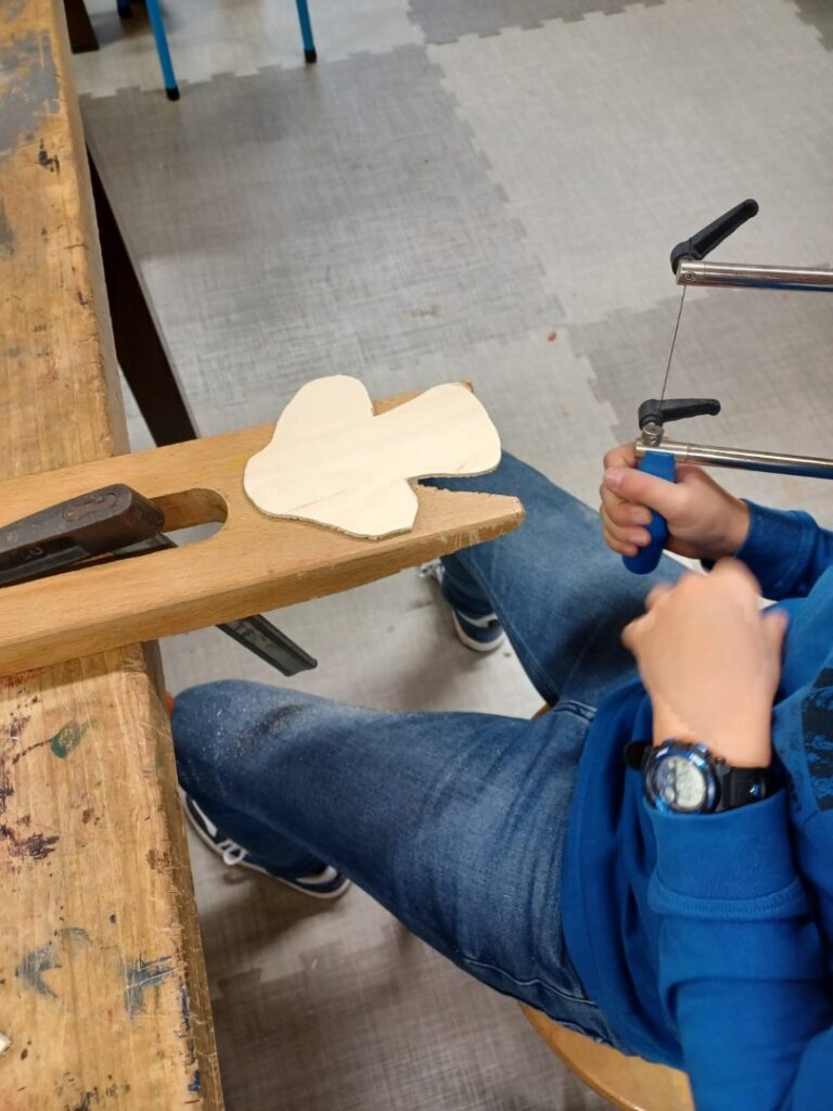 Ein Kind sägt mit einer Laubsäge die Form eines Holzstücks aus, das auf einer Werkbank eingespannt ist.