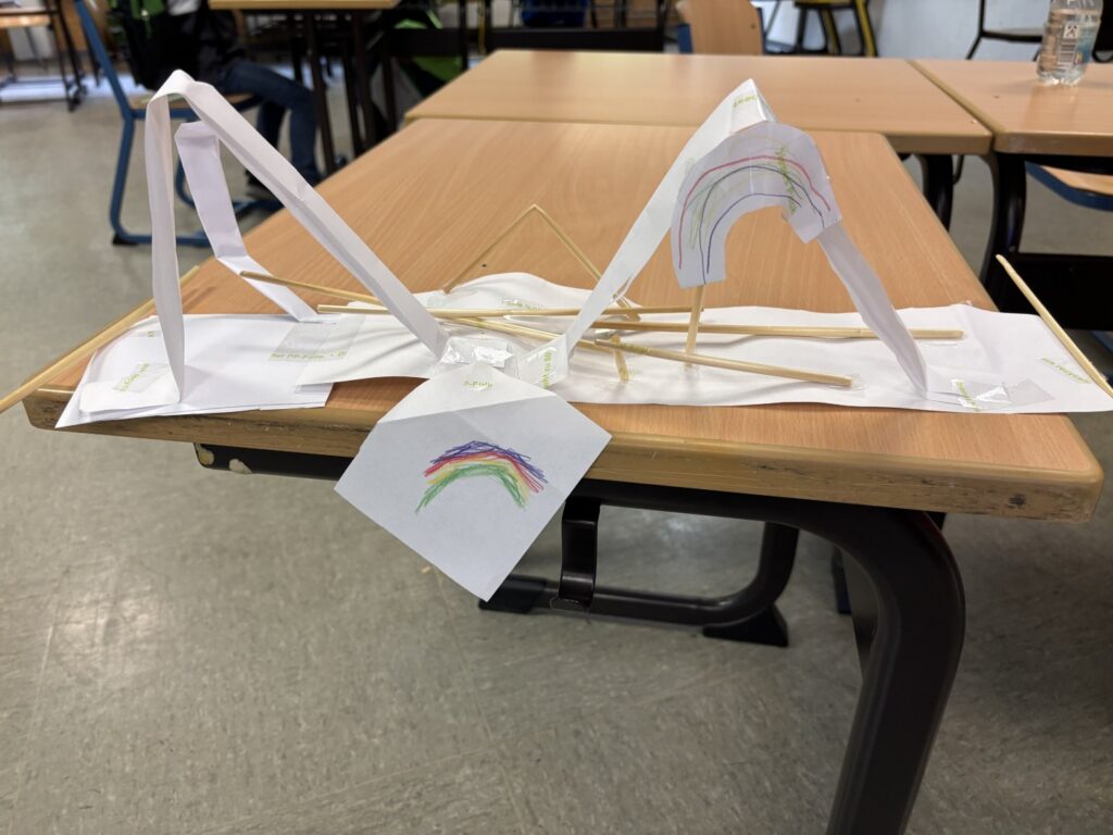 Eine bunte Papierbrücke mit Regenbogenzeichnung verbindet zwei Tische im Klassenraum.