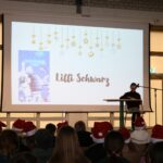 Schülerin liest konzentriert an einem Tisch; im Hintergrund wird das Buchcover „Wie ein springender Delfin“ projiziert.