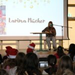 Schülerin liest aus „Tintenherz“ vor, dessen Buchcover deutlich auf der Projektionsfläche angezeigt wird.