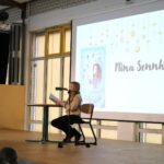 Schülerin liest an einem Stehtisch aus einem Buch; auf der Leinwand ist „Pferdeflüsterer Mädchen – Rubys Entscheidung“ zu sehen.