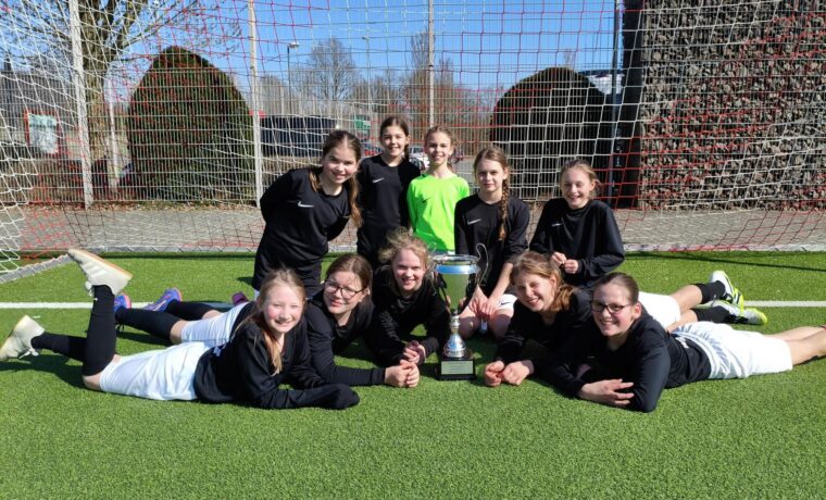 Mädchenmannschaft sitzt zusammen mit Pokal auf dem Fußballfeld.