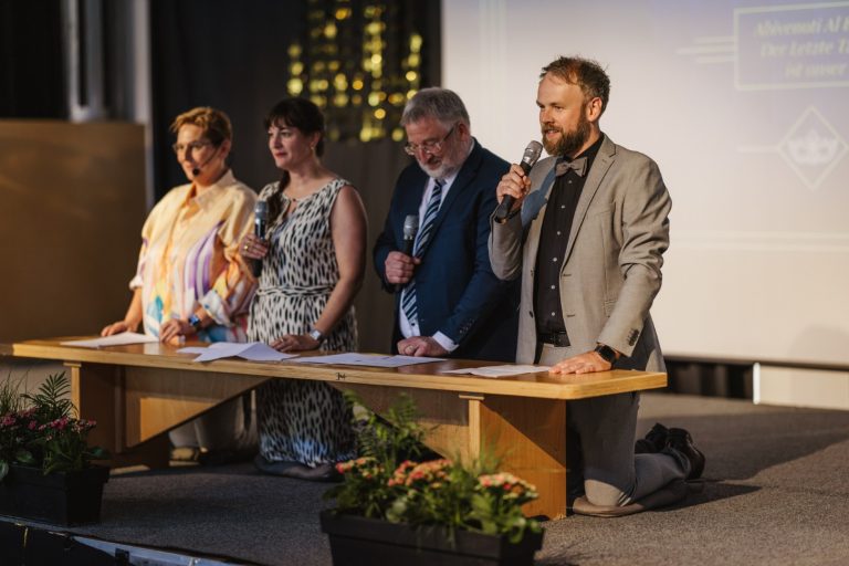 Vier Personen stehen an einem Tisch, während sie ein Dokument präsentieren.