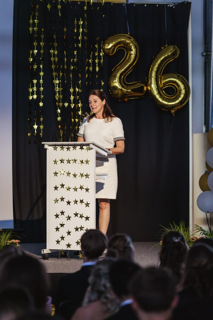 Eine Frau spricht am Rednerpult vor goldenen Ballons mit der Zahl 26.