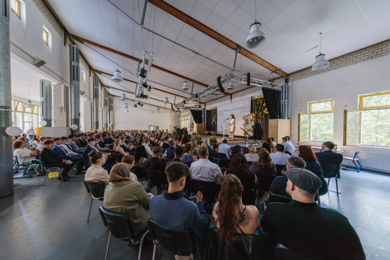 Abschlussveranstaltung mit vielen Gästen in einem festlichen Saal.
